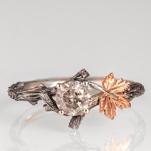 Puede incluir: Un anillo de plata con una gema grande, redonda y de color claro. El anillo presenta una banda en forma de ramita con un acento de hoja de oro rosa. La gema está sujeta por pequeñas garras.