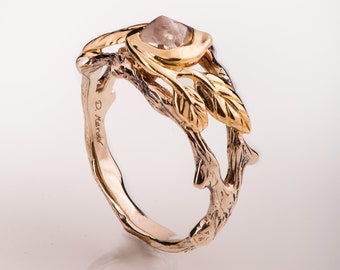 May include: A gold ring featuring a branch design and a pink gemstone. The ring is engraved with the text "D. Karaol".