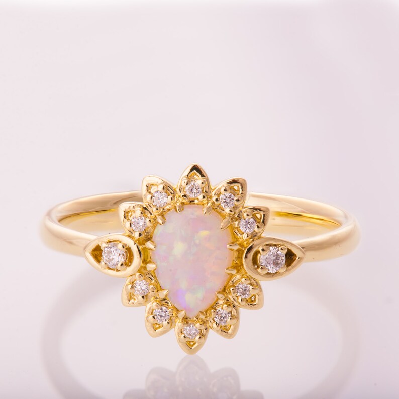 May include: A gold ring with a pear-shaped opal gemstone surrounded by a halo of smaller diamonds. The ring has a delicate floral design.