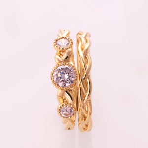 May include: Two gold rings with a braided design. The top ring has three clear round stones set in the band.