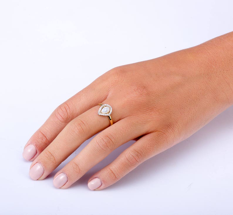 Puede incluir: Un anillo de oro con una piedra clara en forma de pera engastada en un halo de piedras claras m&aacute;s peque&ntilde;as.