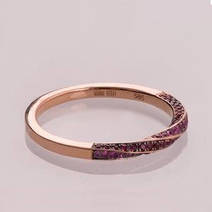 Puede incluir: Un anillo de banda de oro rosa con un diseño retorcido, engastado con una fila de pequeños rubíes rojos. El anillo está grabado con "DORON MENAV" y "585".