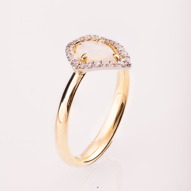 Puede incluir: Un anillo de oro con una piedra de &oacute;palo en forma de pera engastada en un halo de diamantes. El anillo tiene una banda sencilla.