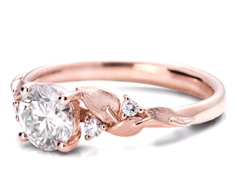 May include: A rose gold engagement ring with a round center stone and smaller accent stones set in a delicate leaf design.
