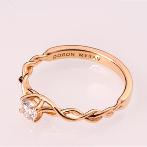 K&ouml;nnte beinhalten: Ein goldener Ring mit einem Diamanten, der in einem verdrehten Band gefasst ist. Der Ring ist mit den Worten "DORON MERAV" graviert.