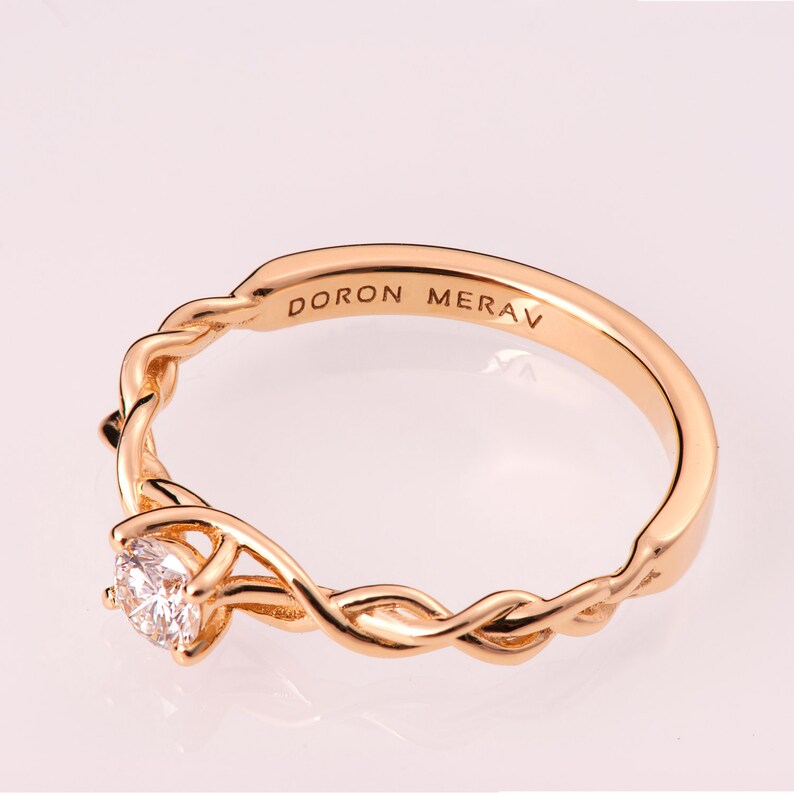 K&ouml;nnte beinhalten: Ein goldener Ring mit einem Diamanten, der in einem verdrehten Band gefasst ist. Der Ring ist mit den Worten "DORON MERAV" graviert.