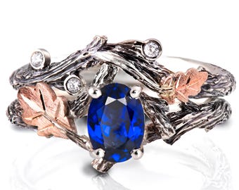 Puede incluir: Un anillo de plata y oro rosa con una piedra preciosa de zafiro azul y detalles de diamantes. El anillo presenta un diseño de ramas y hojas entrelazadas.