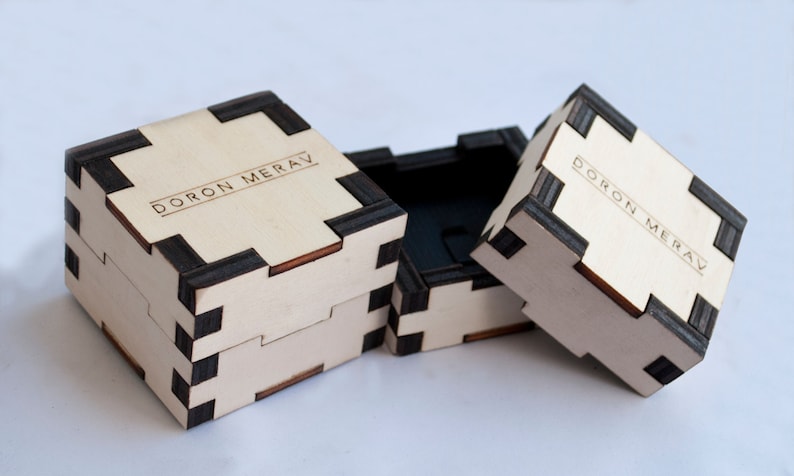 May include: Three wooden boxes with black trim and the text "DORON MERAV" engraved on the top. The boxes are open and stacked on top of each other.