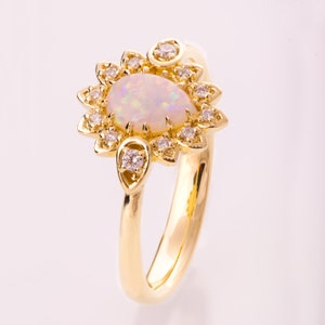 May include: A gold ring with a large oval opal surrounded by a halo of smaller diamonds. The ring has a delicate floral design.