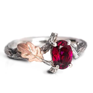 May include: A silver and rose gold ring with a red ruby gemstone set in a branch design with a leaf detail.