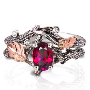 May include: A silver ring with a striking red oval gemstone. The ring has a nature-inspired design with textured branches, small diamonds, and rose gold leaf accents. A unique piece of jewellery.
