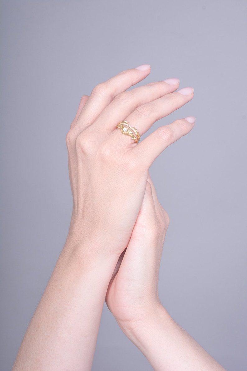 May include: A gold ring with a delicate design featuring small stones. The ring is worn on the middle finger of a hand.
