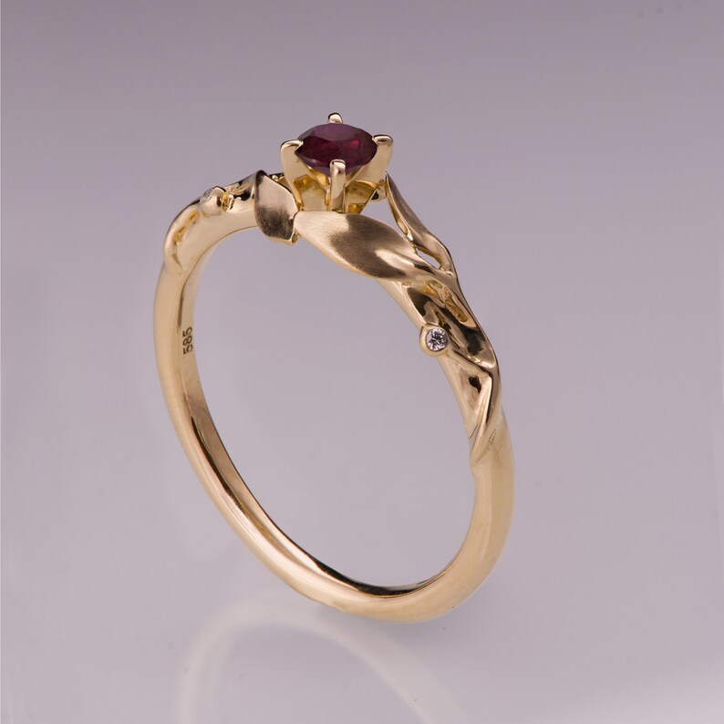 May include: A gold ring featuring a red ruby gemstone and a small diamond accent. The ring has a distinctive, organic design with a twisted band.