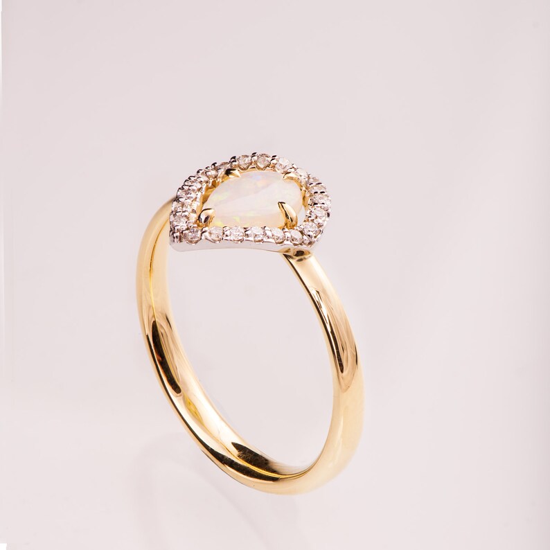 Puede incluir: Un anillo de oro con una piedra de &oacute;palo en forma de pera rodeada por un halo de peque&ntilde;os diamantes.