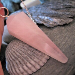 May include: A pink rose quartz crystal pendulum on a silver chain. The pendulum is shaped like a point and is about 2 inches long.