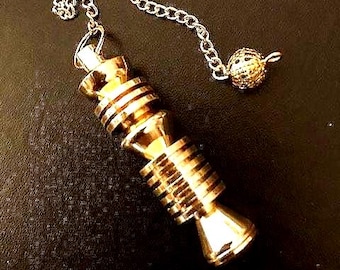 Könnte beinhalten: Ein goldfarbenes Metallpendel mit einem zylindrischen Körper, horizontalen Rillen und einer glatten, konischen Basis. Das Pendel ist an einer feinen goldfarbenen Kette befestigt, die an ihrem Ende eine kleine, texturierte kugelförmige Perle aufweist.