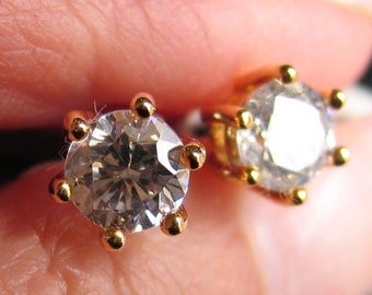 May include: A pair of gold earrings with clear round cubic zirconia stones set in a prong setting.