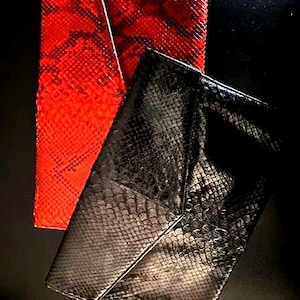 Può includere: Due pochette rettangolari a busta con un motivo testurizzato a pelle di serpente. Una pochette è rosso vivace con dettagli a scaglie scure, mentre l'altra è nera tinta unita con una finitura lucida. Entrambe presentano una chiusura a patta.