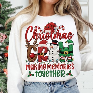 May include: White Christmas-themed sweatshirt with the words "Christmas Crew" in red and brown, featuring a reindeer, Santa hat, snowman, and elf. The phrase "making memories together" is below in red and green.