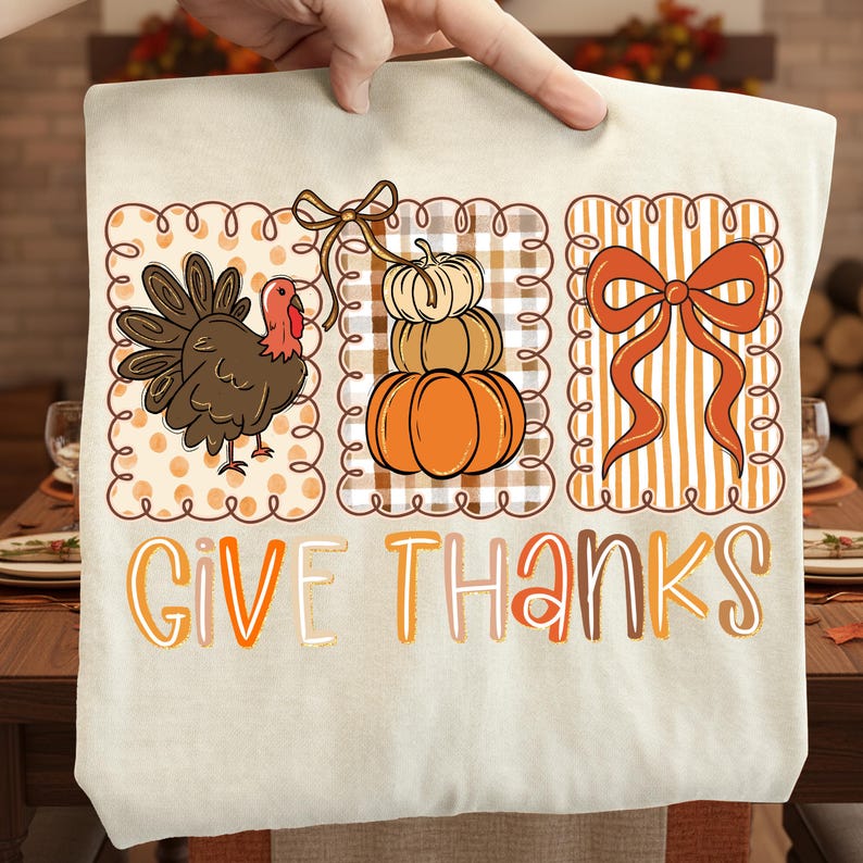 May include: A beige tote bag featuring a Thanksgiving design. The design includes a turkey, stacked pumpkins, and a bow, all within decorative frames. The words "GIVE THANKS" are printed in orange and brown.