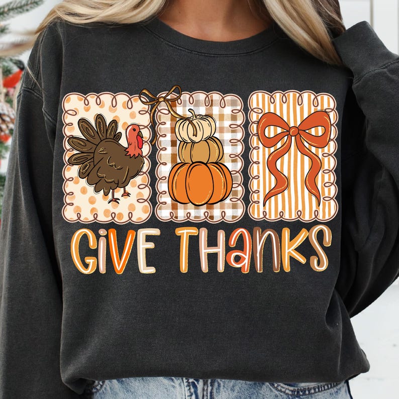 May include: Dark gray sweatshirt with a Thanksgiving-themed graphic. The graphic features a turkey, a stack of pumpkins, and a bow, all within decorative frames. The words "GIVE THANKS" are written in orange and white letters.