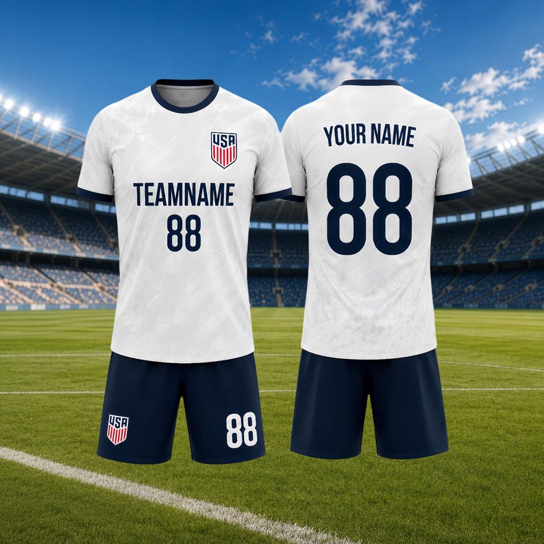 May include: White soccer jersey and shorts set with navy blue accents. The jersey features the USA emblem, team name, and the number 88. The shorts also display the number 88. The background shows a soccer field and stadium.