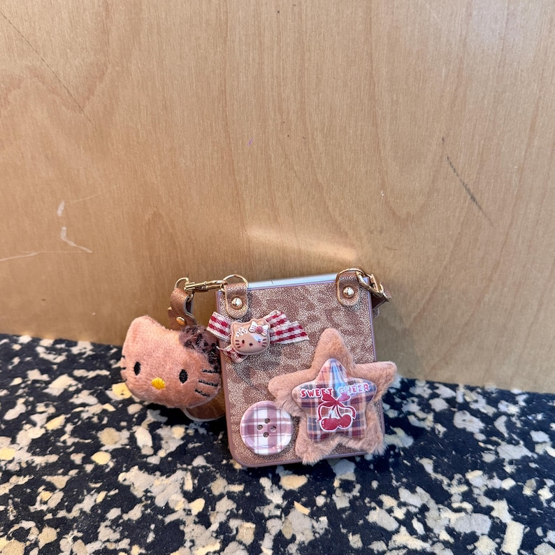 May include: A small, brown purse with a leopard print pattern, adorned with a plush star, a Hello Kitty bow, and a button. A Hello Kitty plush keychain hangs from the purse. The star has the words "Sweet Cherry" on it.