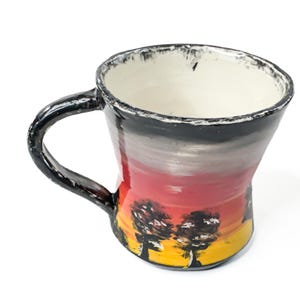 May include: A ceramic mug featuring a hand-painted sunset landscape with a yellow base, orange and red midsection, and a dark grey sky. The mug has a black handle and a white interior with a black, textured, uneven rim around the top edge.