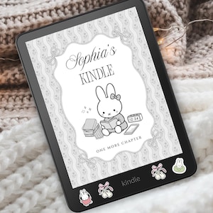 May include: A black e-reader featuring a custom screen display with the text Sophia's KINDLE and ONE MORE CHAPTER, accompanied by a line art illustration of a rabbit reading a book. The device is decorated with small rabbit and bow stickers.