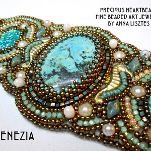 Op de afbeelding: Een turquoise en gouden kralenarmband met een grote turquoise edelsteen in het midden. De armband is gemaakt met kleine kralen en parels en heeft een delicaat, ingewikkeld ontwerp. De tekst "PRECIOUS HEARTBEADS FINE BEADED ART JEWELRY BY ANNA LISZTÉS" en "VENEZIA" zijn zichtbaar op de afbeelding.