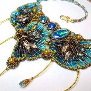 May include: A beaded necklace featuring a butterfly design in shades of blue, gold, and silver. The necklace has a long, dangling chain with multiple beads.