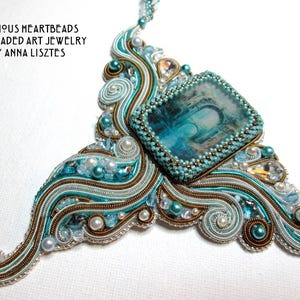 May include: An ornate, handcrafted necklace with a central rectangular pendant featuring a blue and white image. The necklace is adorned with teal, silver, and gold-colored threads, pearls, and beads. The text "PRECIOUS HEARTBEADS FINE BEADED ART JEWELRY BY ANNA LISZTES" is visible.