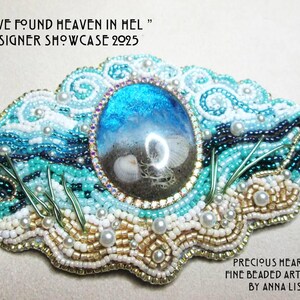 May include: A detailed beaded artwork with a central oval focal point depicting a beach scene. The piece uses blue, turquoise, white, and gold beads. The text "I HAVE FOUND HEAVEN IN HEL" and "DESIGNER SHOWCASE 2025" are included in the design.