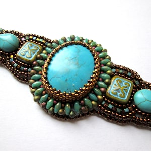May include: A turquoise and gold beaded bracelet with a large turquoise stone in the center. The bracelet is made with a variety of beads, including small round beads, square beads, and teardrop-shaped beads.
