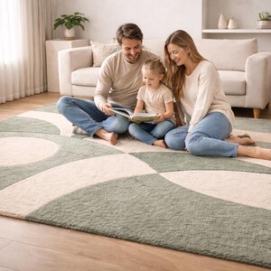 May include: A rectangular area rug featuring a geometric pattern of sage green and cream-coloured interlocking circles and arcs. The rug has a textured pile surface and is positioned on a light-coloured wooden floor in a living room setting.