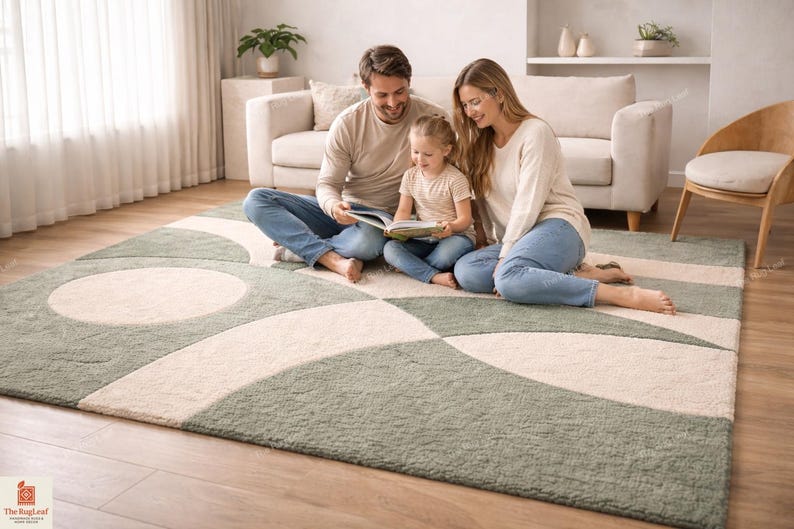 May include: A rectangular area rug featuring a geometric pattern of sage green and cream-coloured interlocking circles and arcs. The rug has a textured pile surface and is positioned on a light-coloured wooden floor in a living room setting.
