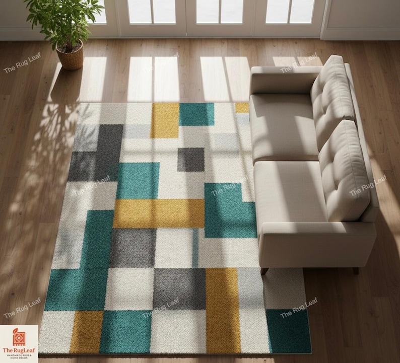May include: Geometric patterned area rug with teal, yellow, gray, and white squares. The rug is rectangular and placed on a hardwood floor, next to a beige sofa. A potted plant is in the upper left corner.