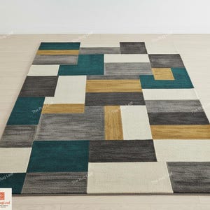 May include: Geometric patterned area rug with teal, gray, gold, and white rectangular blocks. The rug is rectangular and has a modern design, suitable for living rooms or bedrooms. The rug is made of a soft, textured material.