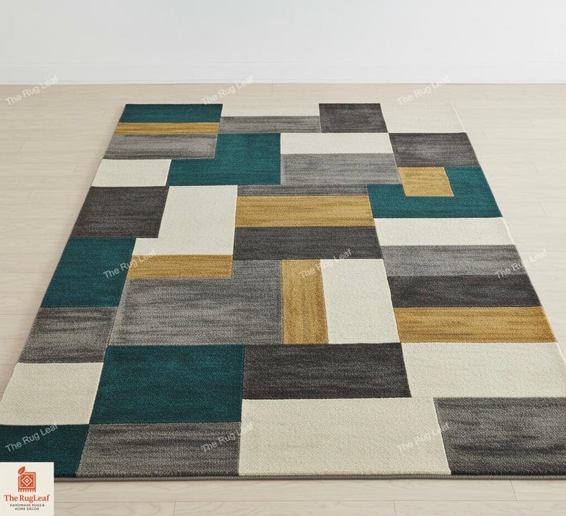 May include: Geometric patterned area rug with teal, gray, gold, and white rectangular blocks. The rug is rectangular and has a modern design, suitable for living rooms or bedrooms. The rug is made of a soft, textured material.