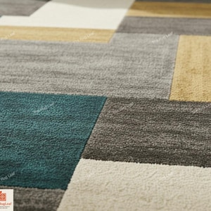 May include: Close-up of a modern area rug with a geometric pattern. The rug features rectangular blocks in shades of gray, teal, beige, and gold. The texture of the rug is visible, suggesting a soft, comfortable material. The Rug Leaf logo is in the bottom left corner.