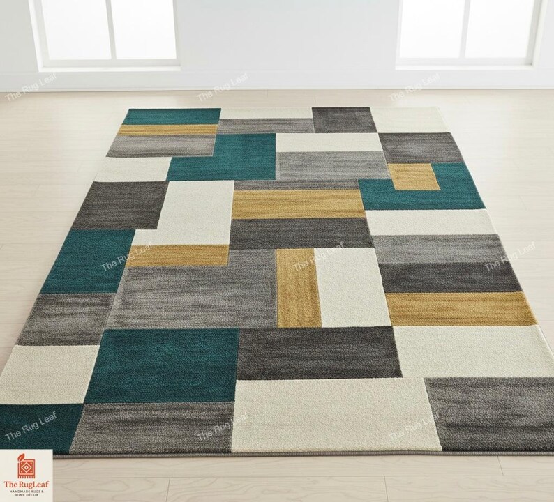 May include: Geometric area rug with a modern design. The rug features rectangular blocks in teal, gray, gold, and off-white. The pattern is a mix of solid and textured sections, creating a contemporary look. The rug is placed on a light wood floor.