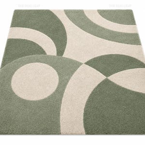 May include: A rectangular area rug featuring a geometric pattern of overlapping circles and arcs in sage green and cream. The rug has a dense, textured pile surface with clean, curved lines that create a repeating abstract design across the entire piece.