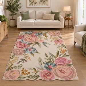 May include: A rectangular area rug with a cream-coloured background featuring a scalloped edge and a floral pattern of large pink roses, blue flowers, and green foliage. The design is distributed along the perimeter of the rug, leaving the centre open.