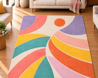 May include: A rectangular area rug featuring a geometric pattern of curved, radiating bands in shades of pink, orange, yellow, teal, and purple against a cream background, with a solid orange circle positioned near the top center of the design.