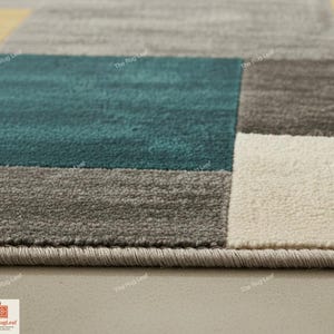 May include: Close-up of a modern area rug with a geometric design. The rug features blocks of teal, gray, and off-white. The edges are finished with a gray border. The Rug Leaf logo is visible in the bottom left corner.