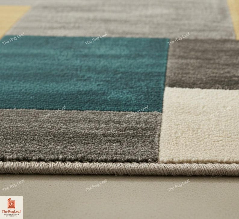 May include: Close-up of a modern area rug with a geometric design. The rug features blocks of teal, gray, and off-white. The edges are finished with a gray border. The Rug Leaf logo is visible in the bottom left corner.