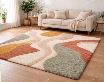 May include: A rectangular area rug with a wavy, abstract design in shades of cream, orange, yellow, and green. The rug is placed on a hardwood floor in front of a beige sofa. The rug's design adds a modern touch to the living room.