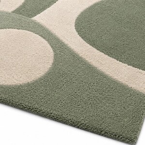 May include: A tufted area rug featuring a geometric pattern of sage green and cream-coloured shapes. The design consists of large circles and curved lines that create a soft, textured surface with a dense pile construction throughout the piece.