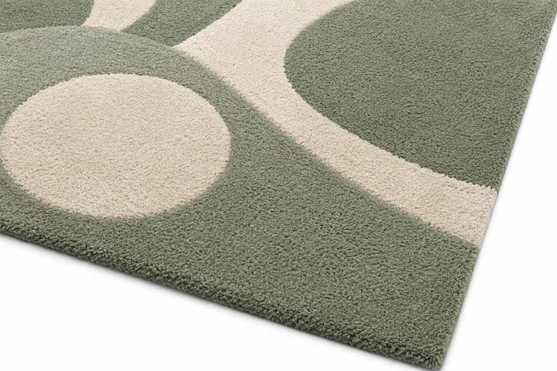 May include: A tufted area rug featuring a geometric pattern of sage green and cream-coloured shapes. The design consists of large circles and curved lines that create a soft, textured surface with a dense pile construction throughout the piece.