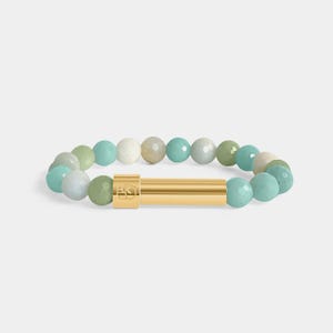 May include: A beaded bracelet featuring a mix of light green, blue, and white round beads. The bracelet has a gold-colored cylindrical clasp. The beads are strung together to form a complete circle.